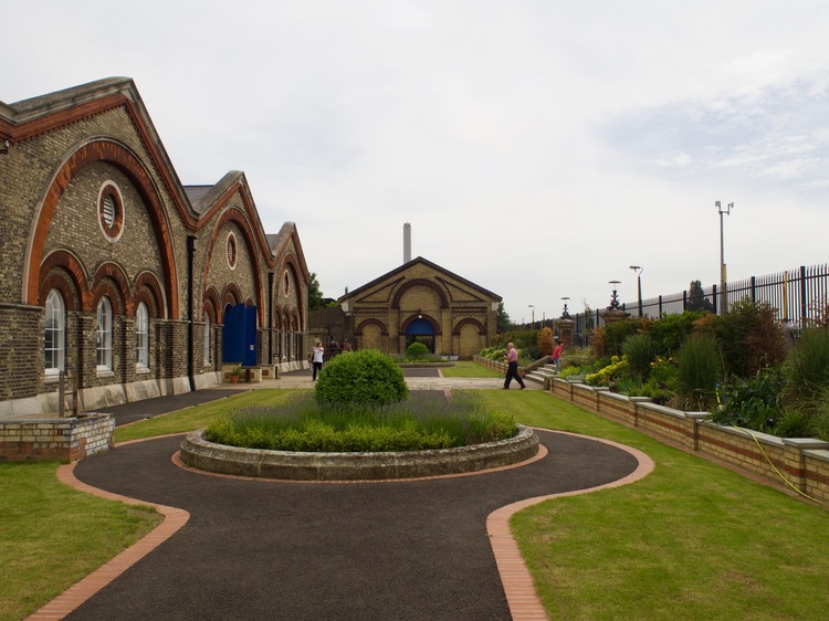 Looking onto a courtyard area with three buildings to the left, some grassy patches and another arched building in the distance.